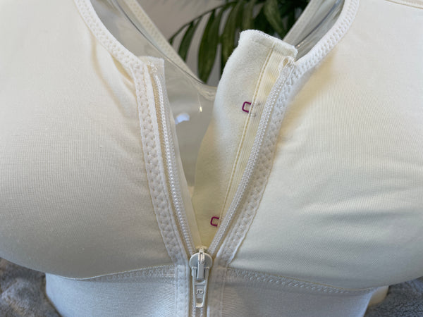 Close up picture of our post-surgery bra, Cara, showcasing the zip. The Cara bra includes a zip and adjustable straps to help with recovery. Cara is a white compression bra designed for comfort and support following surgery. 