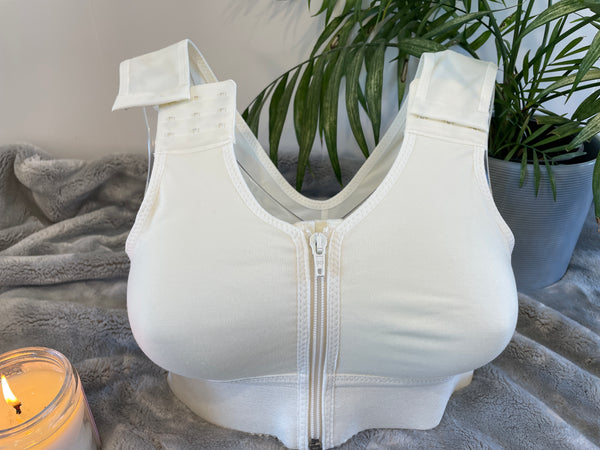 Front on picture of our post-surgery bra, Cara, showcasing the adjustable strap. The Cara bra includes a zip and adjustable straps to help with recovery. Cara is a white compression bra designed for comfort and support following surgery. 