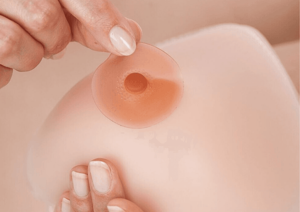 Skin-toned adhesive breast prosthesis nipple being applied to a prosthetic breast. Available in customizable sizes and colors.