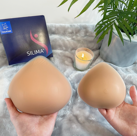 Picture of two Silima Soft & Light Symmetrical Breast Forms of different sizes. The breast form on the left is larger while the one on the right is smaller. In the back of the image is a box with the Silima logo to store the breast form. 