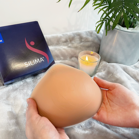 Image of Silima's Soft & Light Super Soft Breast Form (Front). In the background there is a box with the Silima logo to store the breast form. 